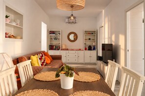 Ein Essbereich mit Holztisch, gewebten Platzsets, einer Zimmerpflanze und weißen Schränken.