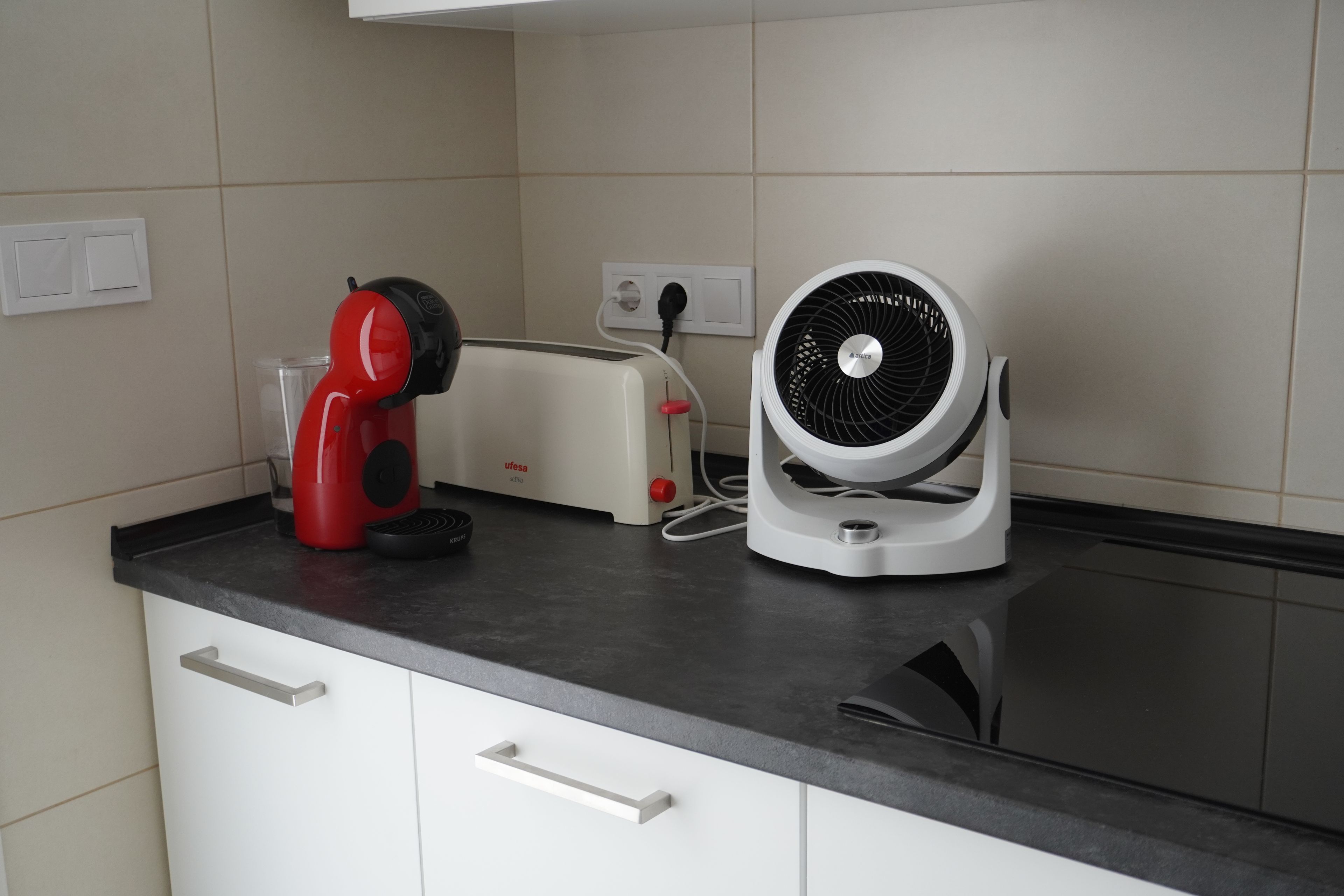 A kitchen with a toaster, a red appliance, and a white fan on the counter.