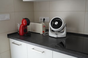 Une cuisine avec un grille-pain, un appareil électroménager rouge et un ventilateur blanc posé sur le comptoir.
