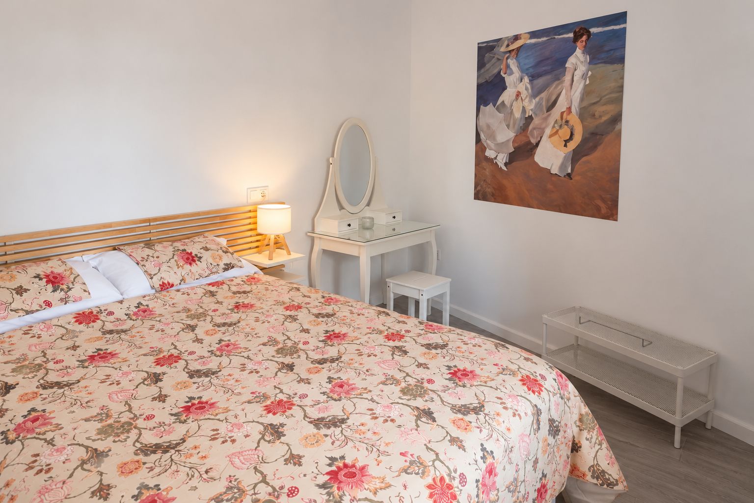 A bedroom with a bed, a bedside table with a lamp, a dresser, a mirror, and a painting on the wall.