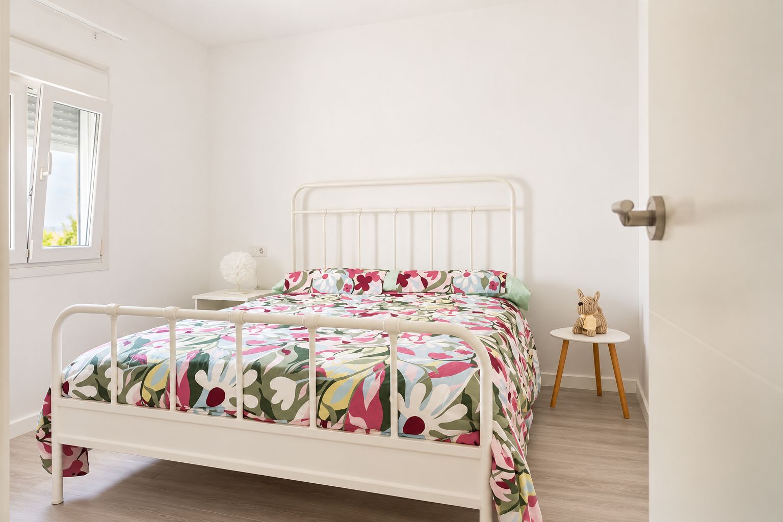 Une chambre à coucher avec un lit, une table de chevet et une petite table ronde sur laquelle est posé un jouet en peluche.