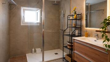 A modern bathroom with a glass-enclosed shower, a wooden vanity with a mirror, and a shelf with toiletries.