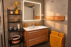 Ein modernes Badezimmer mit Waschtisch, Spiegel und Regalen.
