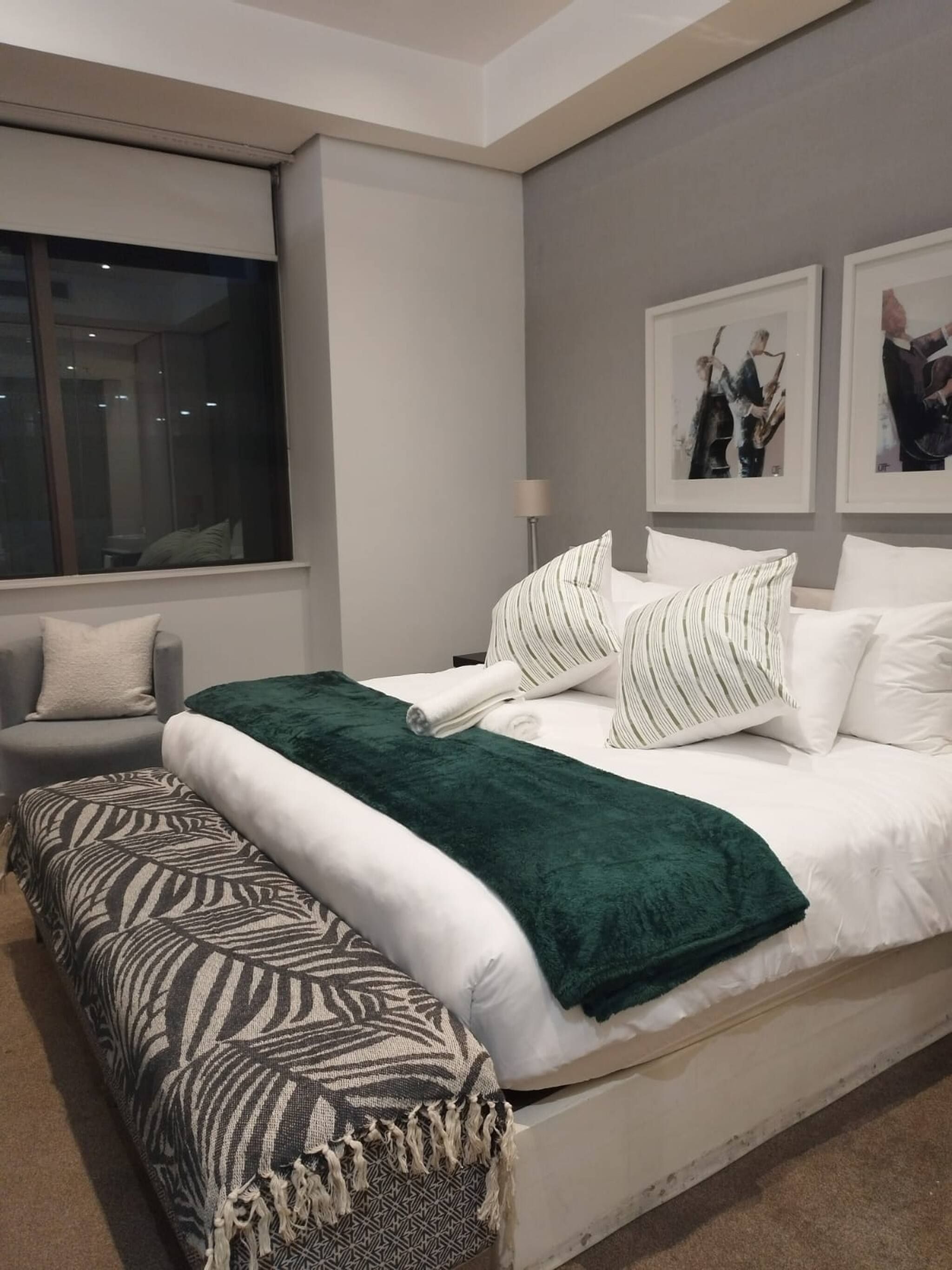 Un dormitorio moderno con una cama grande, un banco, una ventana y obras de arte en la pared.