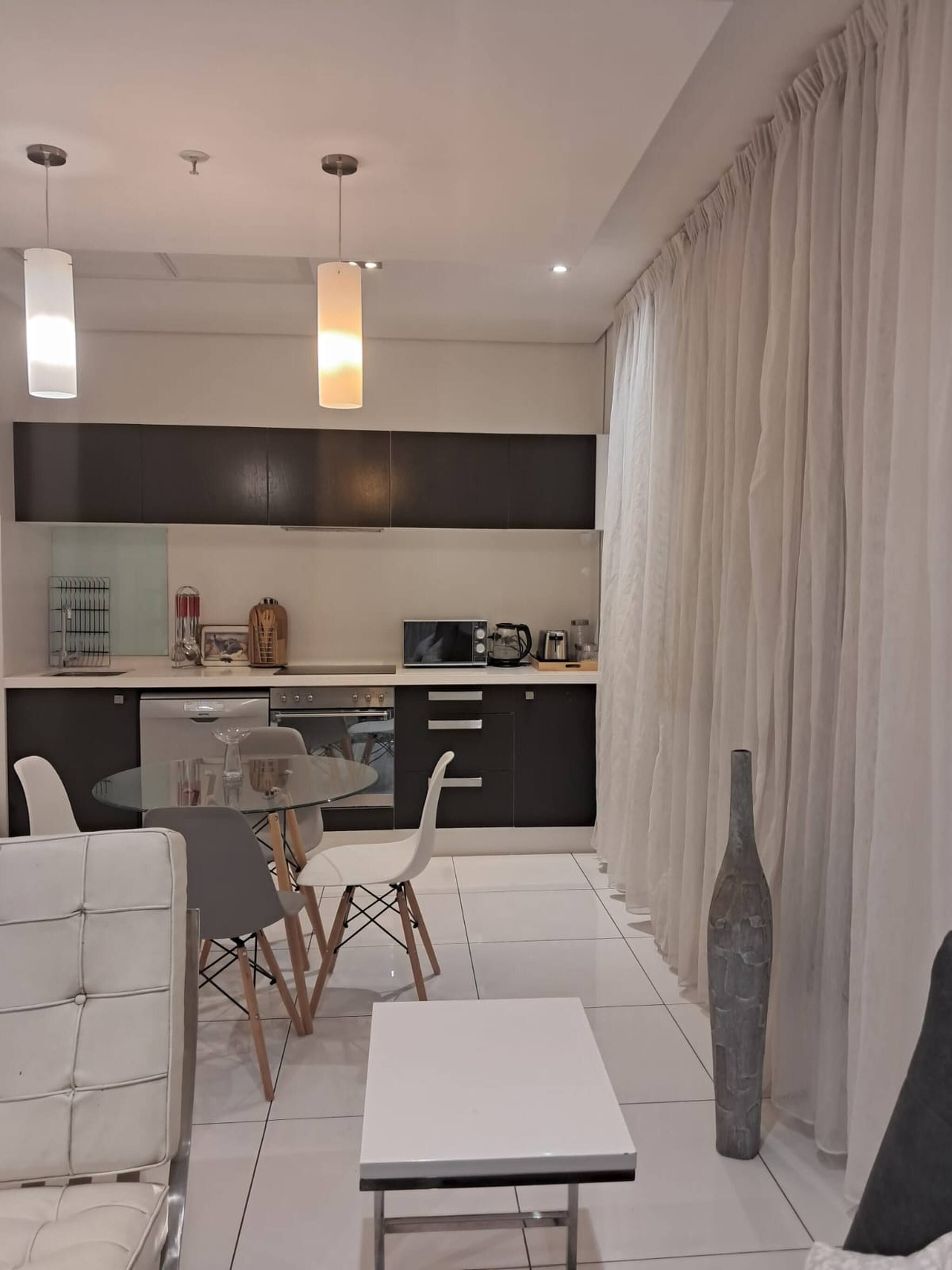 Una cocina moderna con comedor, que incluye una mesa de vidrio, sillas blancas y una mesa blanca.