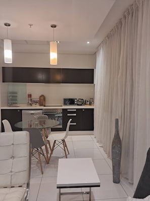 Cozinha moderna com área de jantar, apresentando uma mesa de vidro, cadeiras brancas e uma mesa clara.