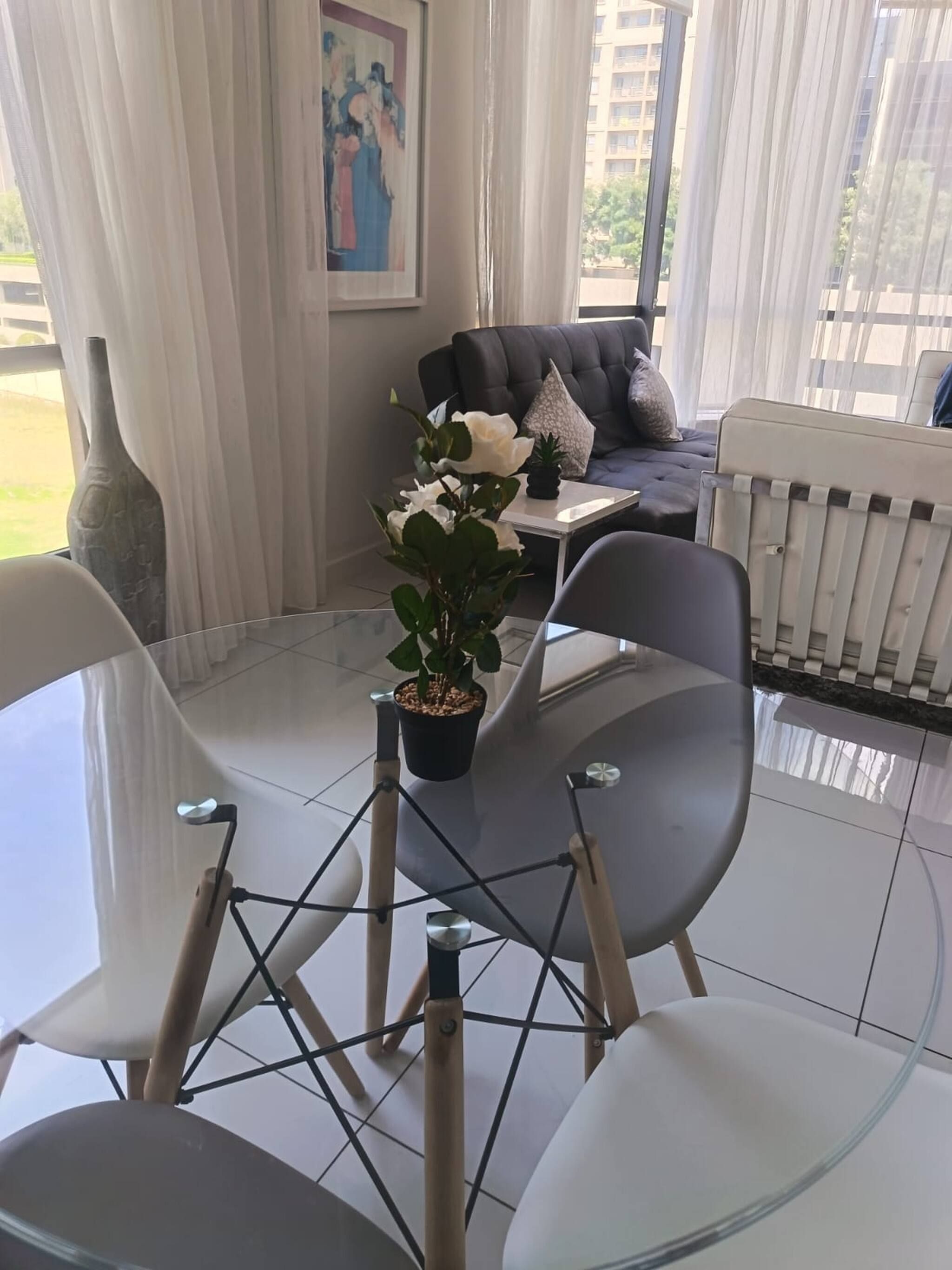 Una sala de estar moderna con una mesa de vidrio, dos sillas, un sofá y una planta en maceta.