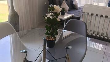 Una sala de estar moderna con una mesa de vidrio, dos sillas, un sofá y una planta en maceta.