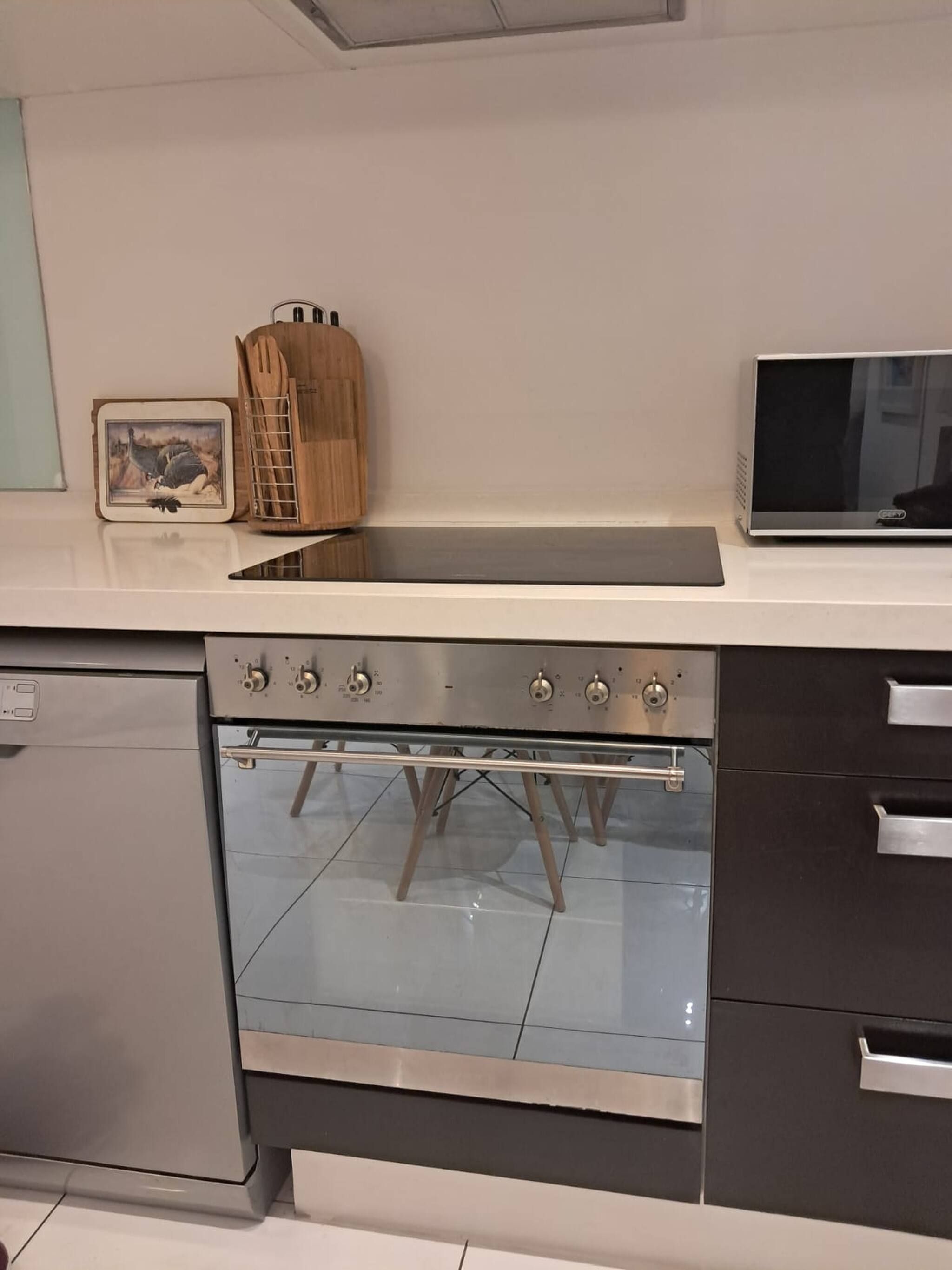 Une cuisine équipée d’un four encastré, d’un four à micro-ondes et d’un porte-ustensiles en bois.
