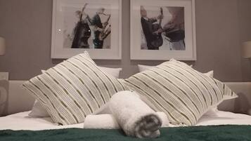 Una cama con almohadas a rayas y una toalla enrollada, cuadros en la pared y una manta verde.