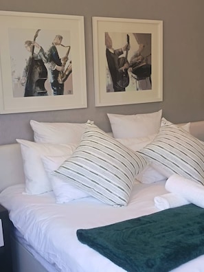 A bed with white bedding and striped pillows, a green throw blanket, and two framed pictures on the wall. - Stylish Sandton Apartment With Stunning City Views (Johannesburg)