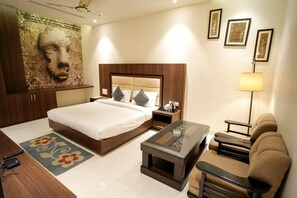 Una habitación de hotel con una cama, mesitas de noche, una mesa de centro, un sofá, una lámpara y obras de arte en las paredes.