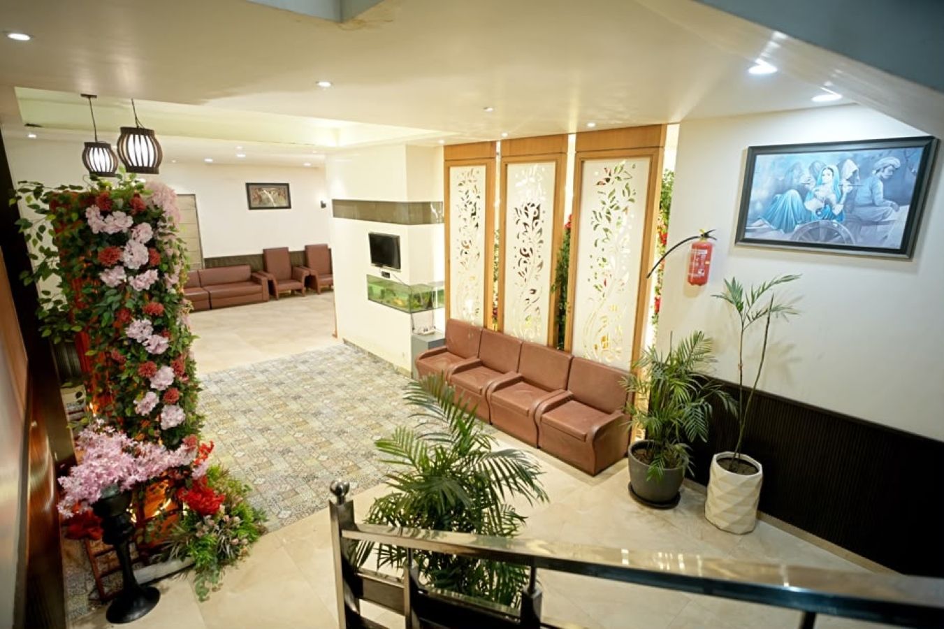 A hotel lobby with a staircase, seating area, decorative plants, and a framed artwork on the wall.