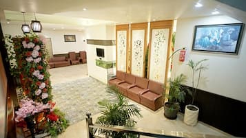 A hotel lobby with a staircase, seating area, decorative plants, and a framed artwork on the wall.