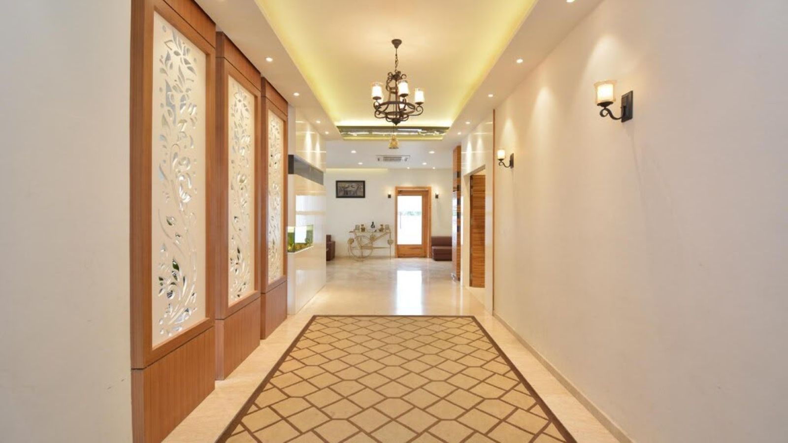 Un couloir d’hôtel avec un sol à motifs, des panneaux décoratifs, un lustre et des appliques murales.