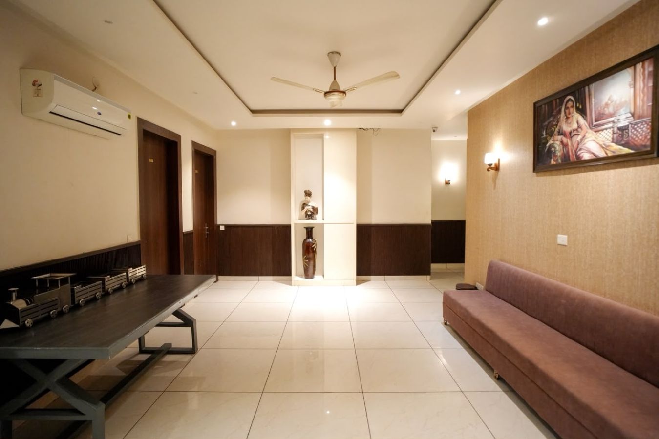 A hotel lobby with a long reception desk, a seating area, a ceiling fan, and a wall-mounted air conditioning unit.