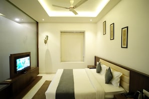 Una habitación de hotel con una cama, televisión, ventilador de techo y ventana.