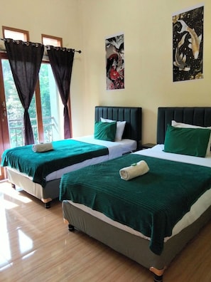 Ein Hotelzimmer mit zwei Betten, jeweils mit grüner Bettwäsche und weißen Kissen, einem Holzboden und einem Fenster mit Vorhängen.