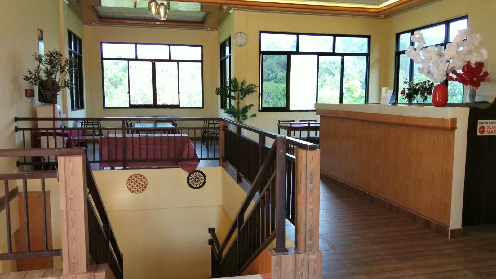 Un vestíbulo de hotel con mostrador de recepción, una escalera y grandes ventanales que ofrecen vistas a zonas verdes exteriores.