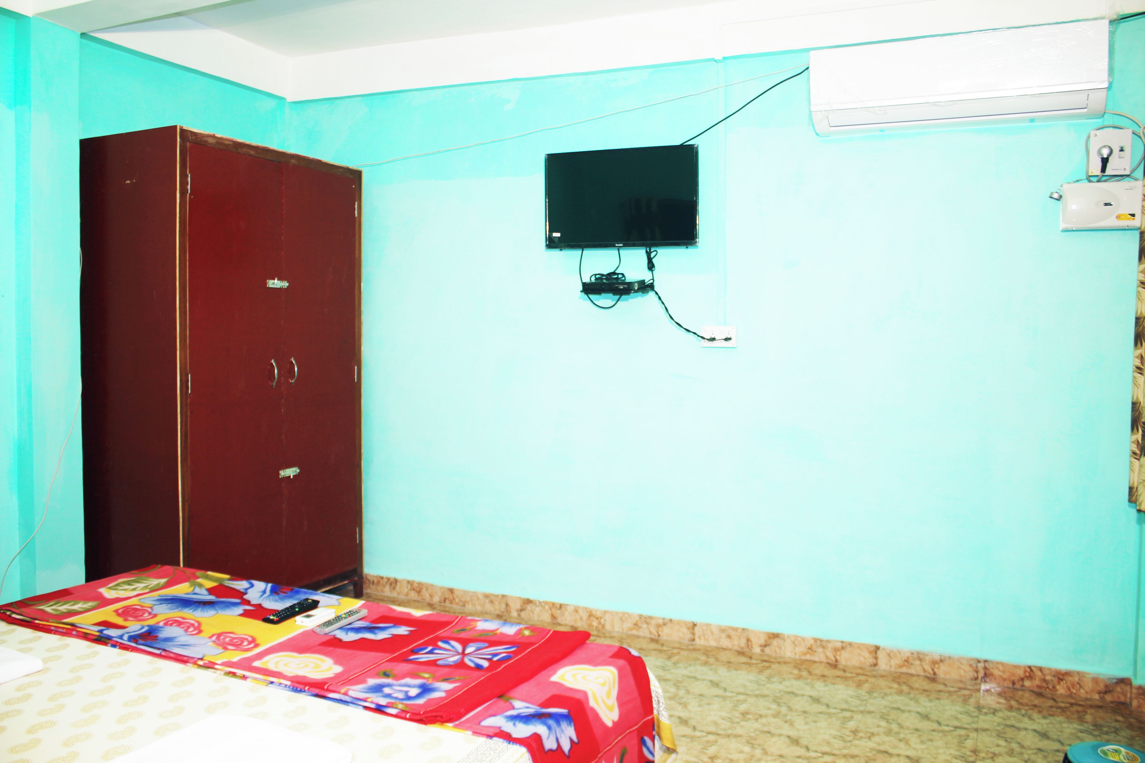 A room with a bed, a wardrobe, a wall-mounted TV, and an air conditioning unit.