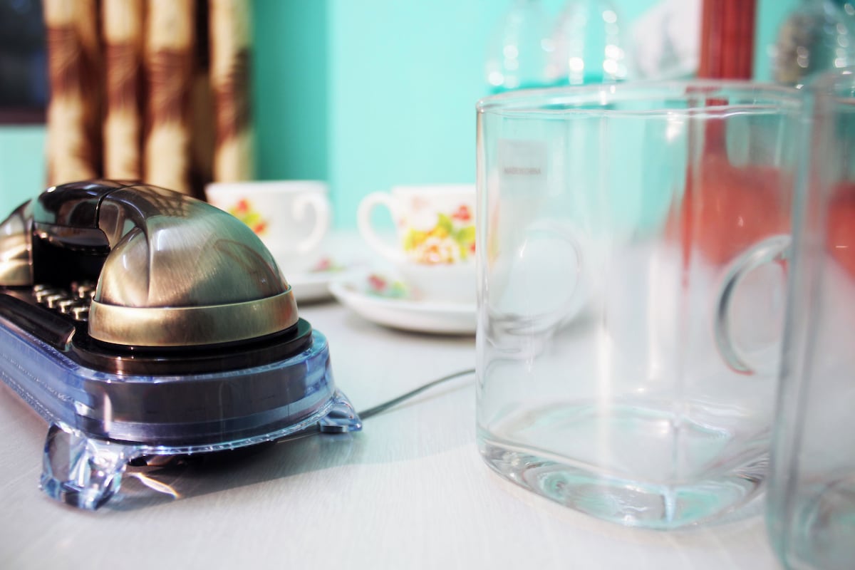 Un teléfono antiguo, una jarra de cristal transparente y un juego de tazas de té con motivos florales sobre una mesa.