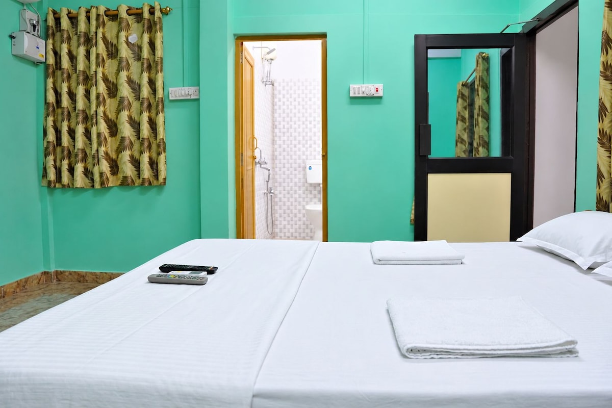 Camera d'albergo con un letto, due telecomandi, un asciugamano piegato e zona doccia visibile attraverso una porta aperta.