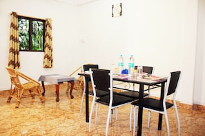A dining area with a table set for four, surrounded by chairs, a window with curtains, and a clock on the wall. - The Lotus Home (Sri Vijaya Puram)