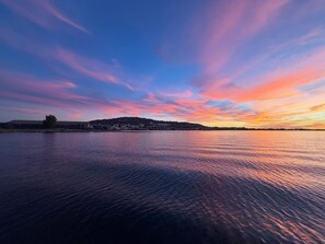 Ruhige Wasserfläche mit einer fernen Küstenlinie und einem farbenprächtigen Himmel.