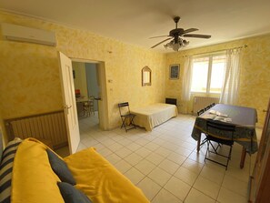 Quarto com cama, escrivaninha, cadeira, ventilador de teto e janela com cortinas.