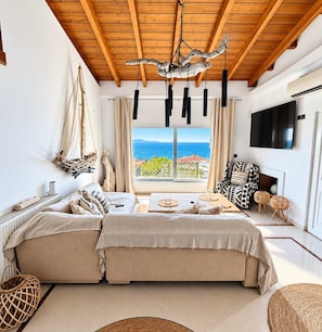 Una habitación con una cama grande, televisión, mesa de comedor y vista al mar.