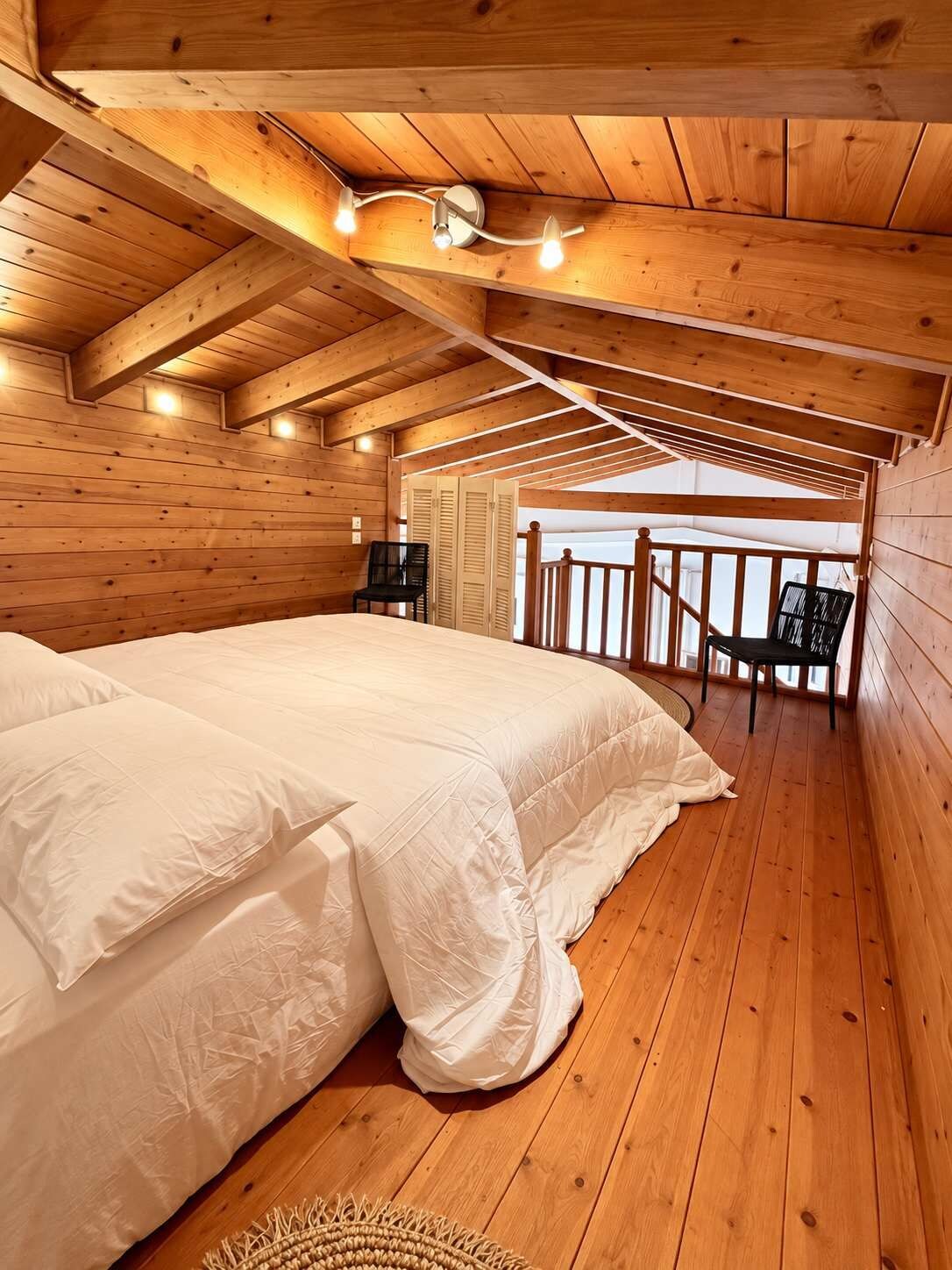 Camera da letto in una baita di legno, con un letto, sedie e un balcone.