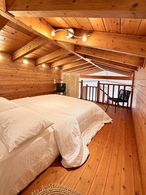 Un dormitorio de cabaña de madera con cama, sillas y un balcón.