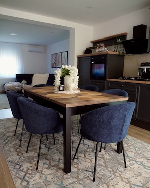Un comedor con una mesa de madera, sillas azules y una cocina al fondo.