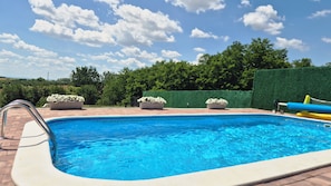 Una piscina con superficie de agua azul cristalina, rodeada por una terraza de ladrillo. Hay tres macetas con flores blancas sobre la terraza.
