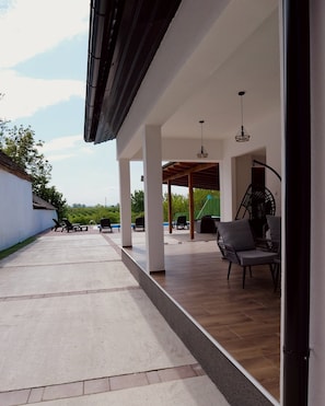 A covered outdoor area with lounge chairs, a pergola, and a view of the landscape.