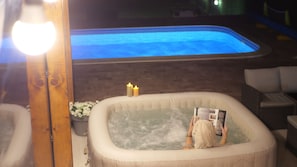 A hot tub with a person reading a magazine, surrounded by a brick wall and a white chair.