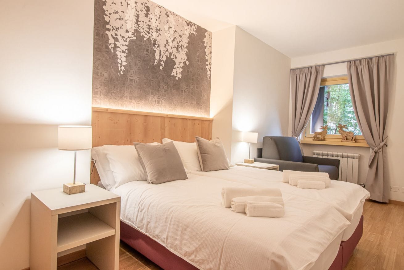Une chambre d’hôtel avec un grand lit, deux tables de chevet, un bureau et une fenêtre avec des rideaux.