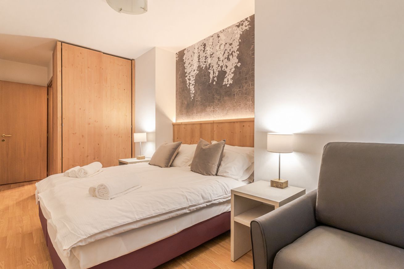 Une chambre d’hôtel comprenant un lit, des tables de chevet, une chaise, une armoire et un mur orné d’un motif texturé.