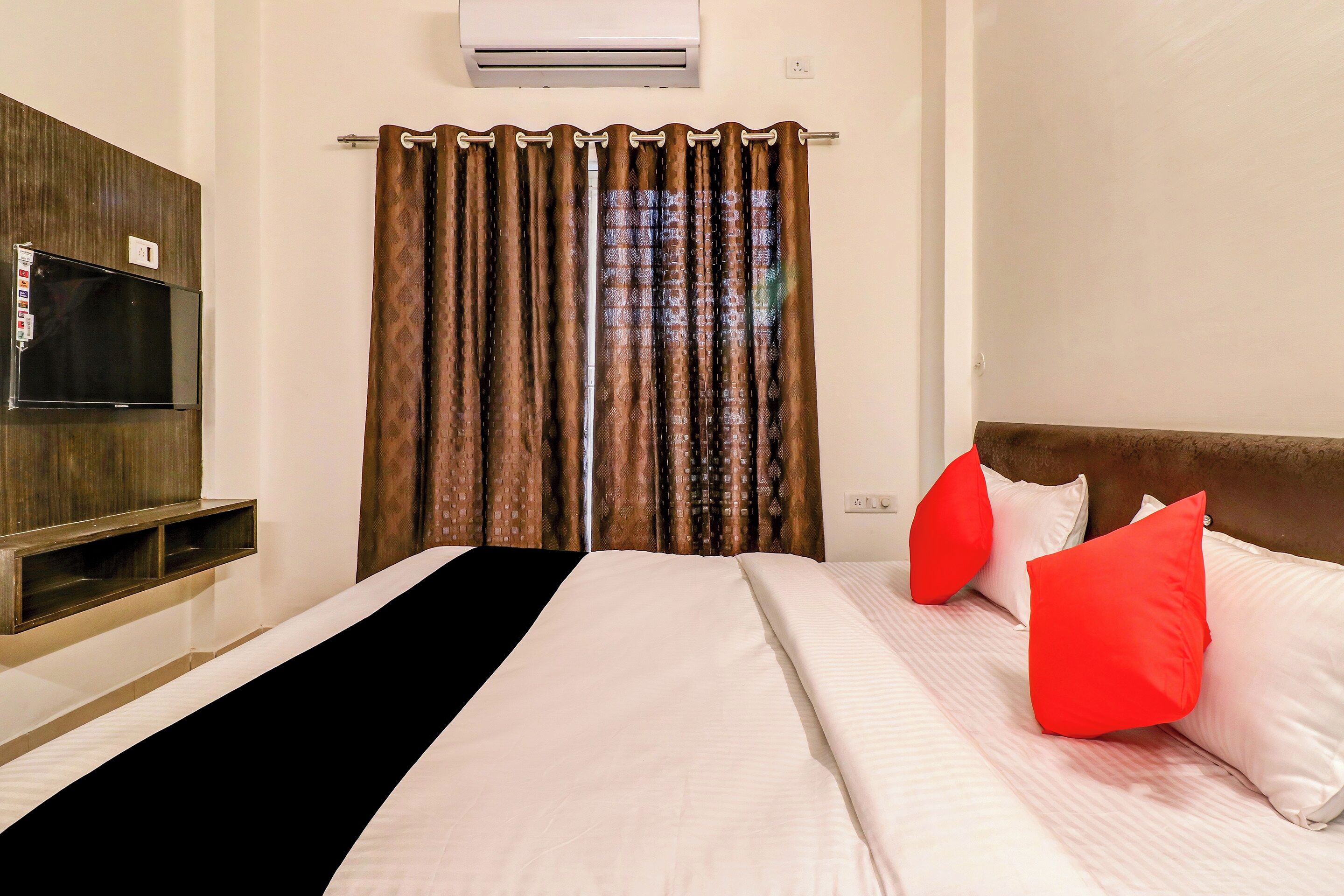 Une chambre d’hôtel avec un lit, un téléviseur à écran plat fixé au mur et une fenêtre avec des rideaux.
