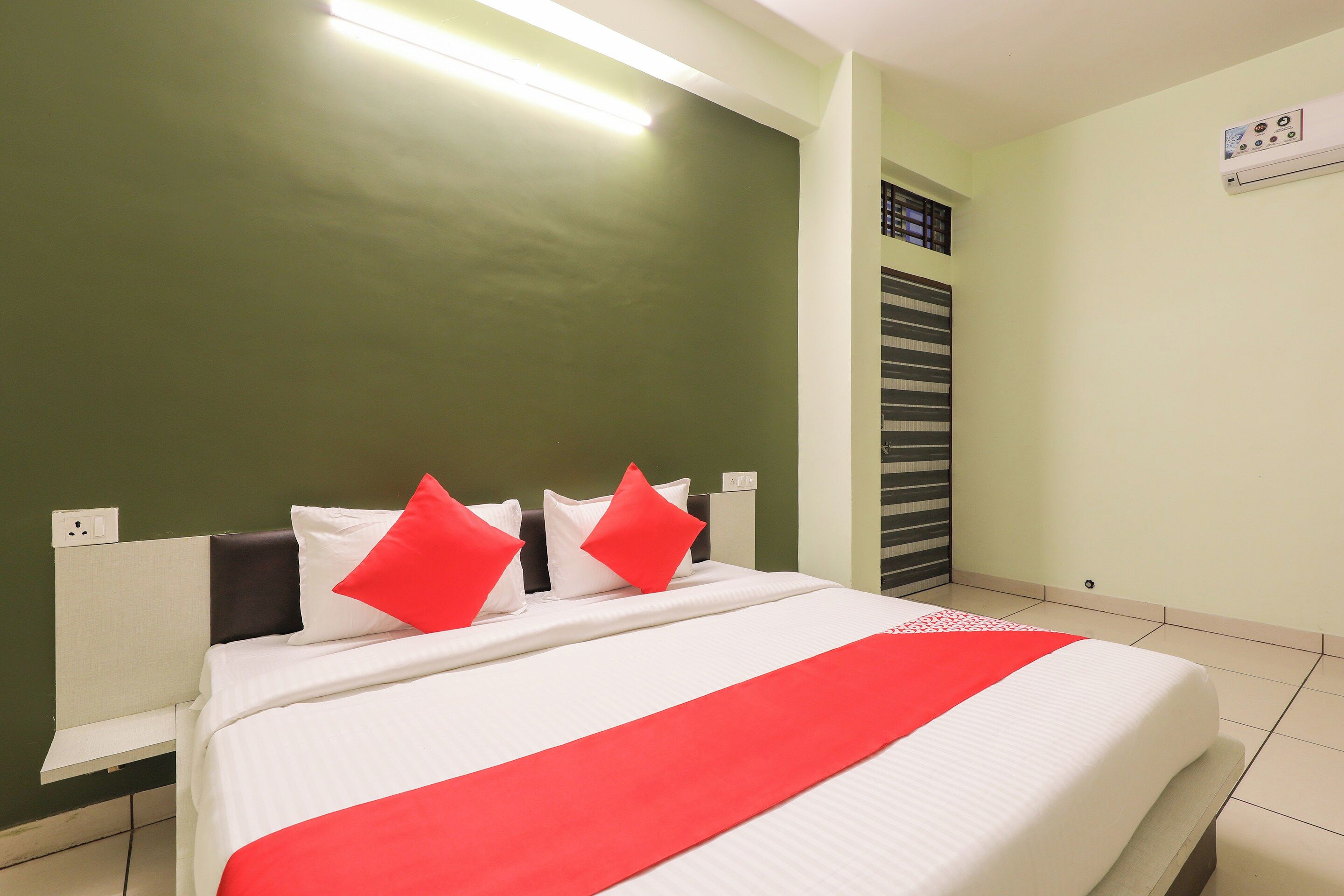 Ein Hotelzimmer mit einem Bett, einem Nachttisch, einer Wand-Klimaanlage und einem Fenster mit Jalousien.