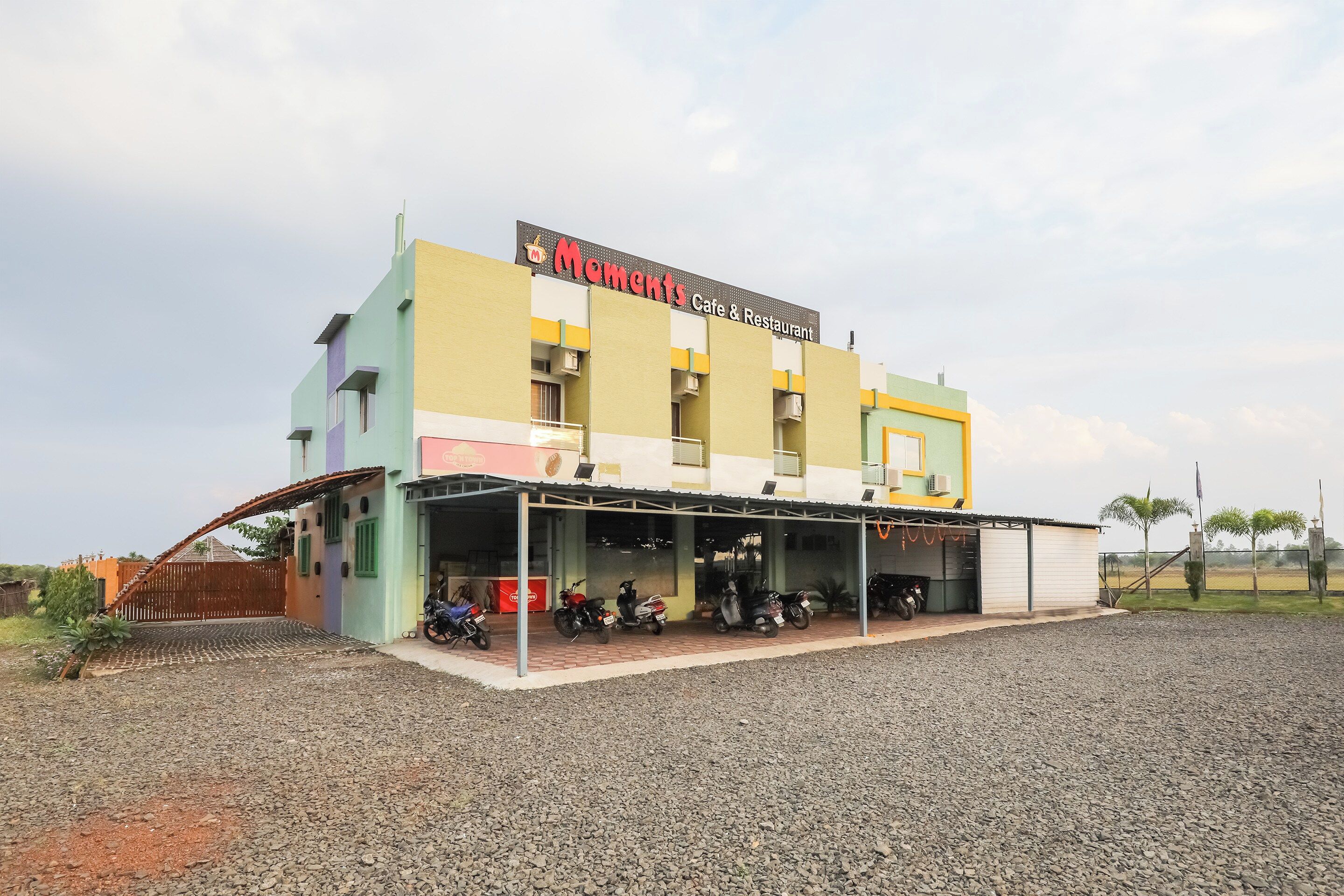 Ein mehrgeschossiges Gebäude mit Café und Restaurant im Erdgeschoss, inklusive überdachter Parkzone für mehrere Motorräder.