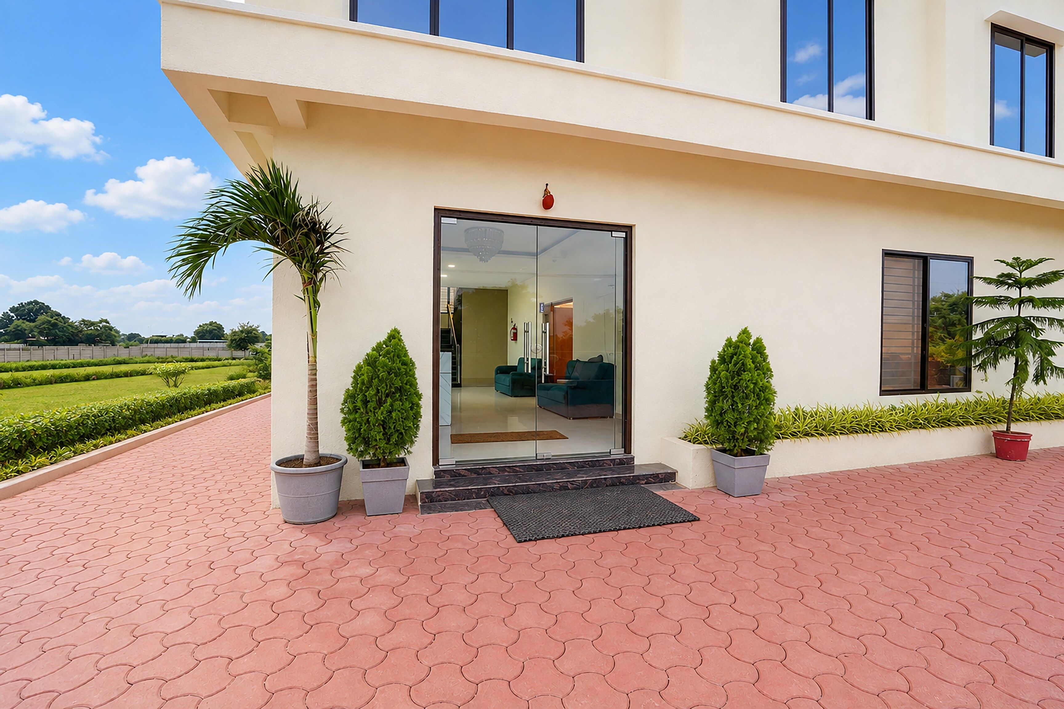 A modern building with a glass door entrance, potted plants, and a paved walkway.