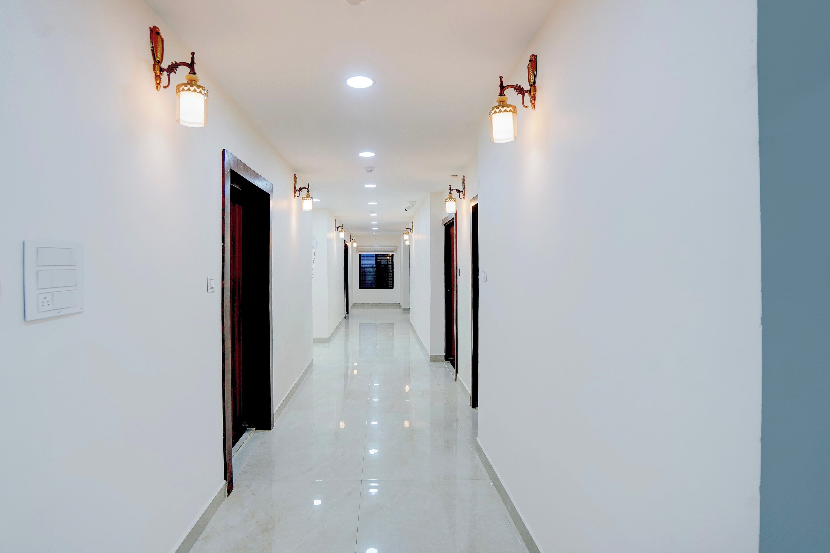 Un pasillo con paredes blancas, luces empotradas en el techo y puertas a ambos lados.