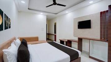 Ein Hotelzimmer mit einem Bett, einem Schreibtisch, einem Fernseher und einem Deckenventilator.