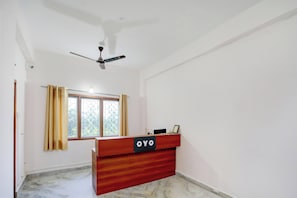 Ein Zimmer mit einer Rezeption mit dem Schild 'OYO', einem Deckenventilator, einem fenster mit Vorhängen und einem Marmorboden.