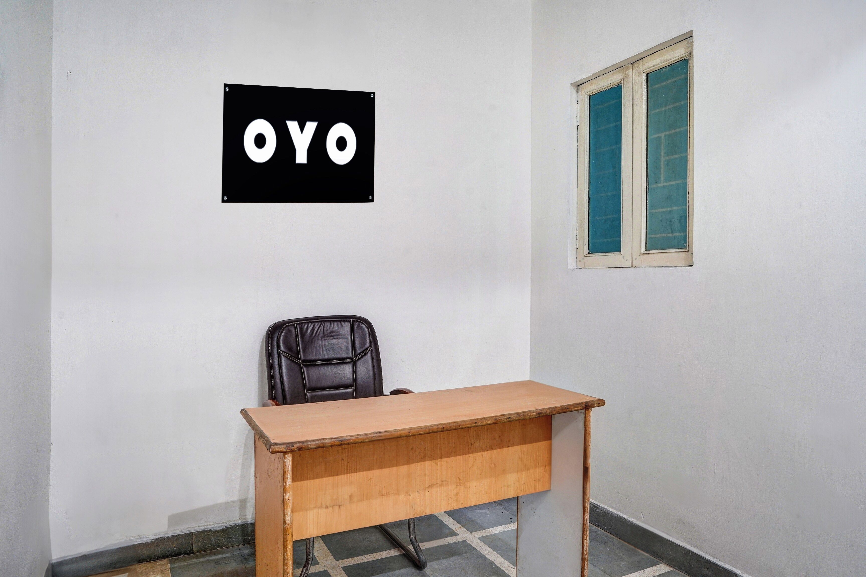 Ein Zimmer mit Schreibtisch, Stuhl, Fenster mit blauen Rollläden und einem an der Wand befestigten Schild mit den Buchstaben 'OYO'.