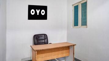 Ein Zimmer mit Schreibtisch, Stuhl, Fenster mit blauen Rollläden und einem an der Wand befestigten Schild mit den Buchstaben 'OYO'.