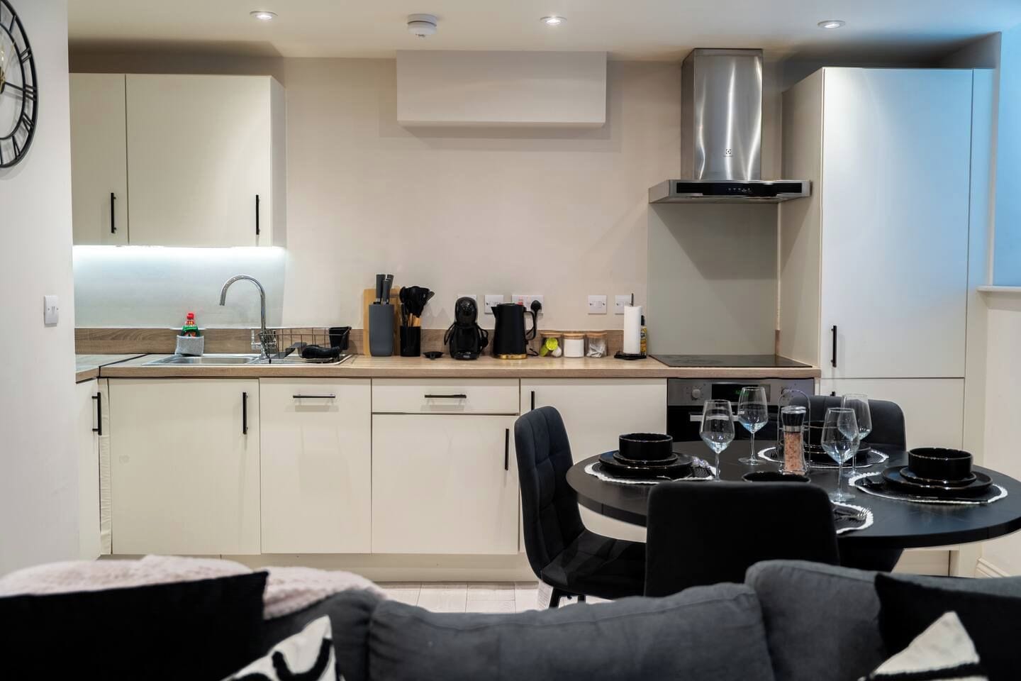 A modern kitchen with white cabinets, a stainless steel range hood, and a dining area with a round table and black chairs.