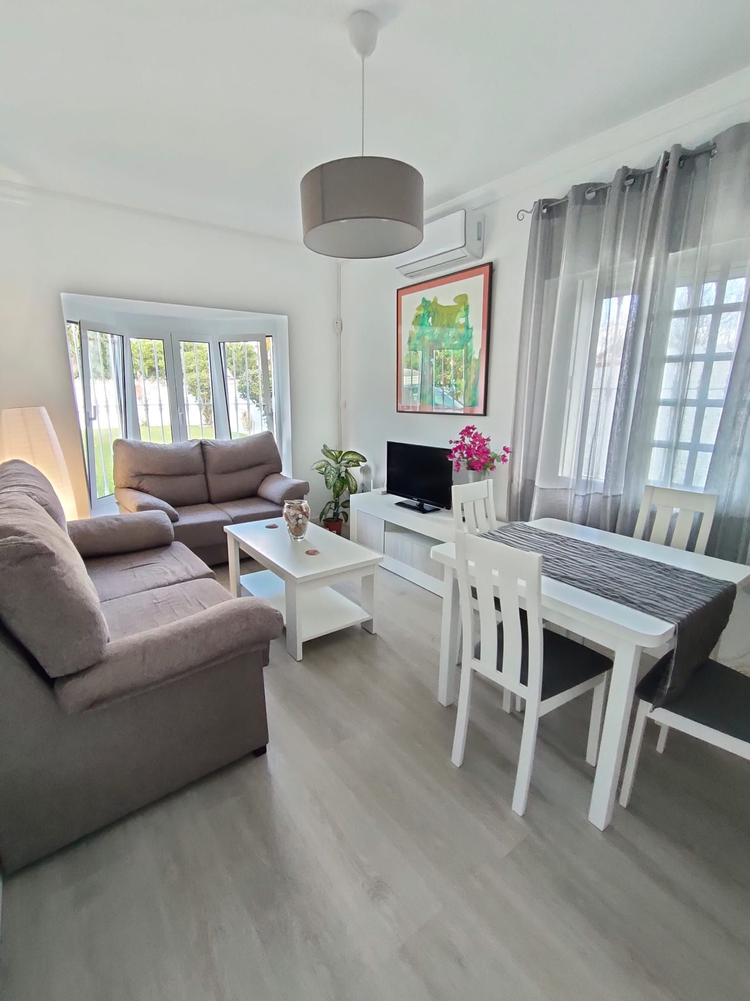 A modern living room with a sofa, a coffee table, a TV, and a dining area with chairs and a table.
