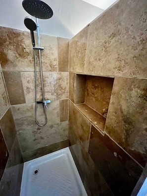 Un espace douche équipé d’un pommeau de douche à main, d’un robinet mural et d’un sol carrelé.